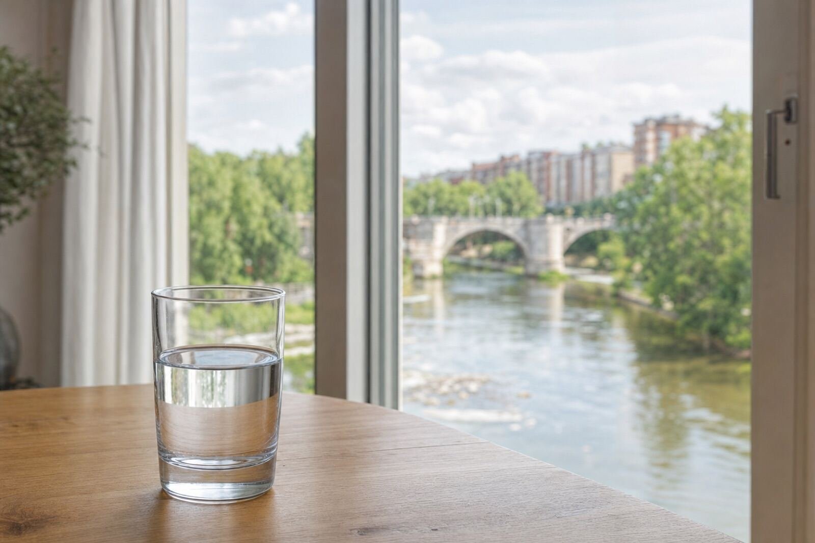 Vaso de agua en una mesa con vistas al río y a un puente de piedra en Valladolid